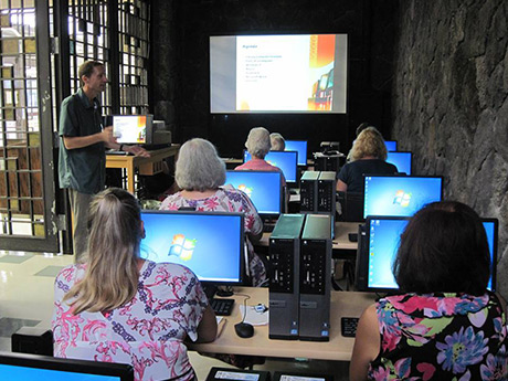 People at desks looking at computers with an instructor standing in the front of the room near a screen