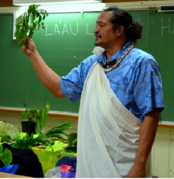 hawaiian man holding a plant in front of a chalkboard