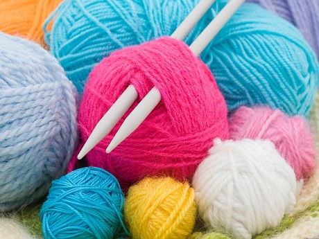 Knitting needles surrounded by balls of colorful yarn.