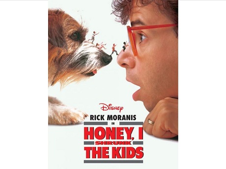 A picture of a dog and man nose to nose looking at each others faces. Miniature sized teenagers are walking across the dog's nose to the man's nose.