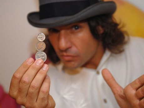 magician in black hat balancing three coins in the air