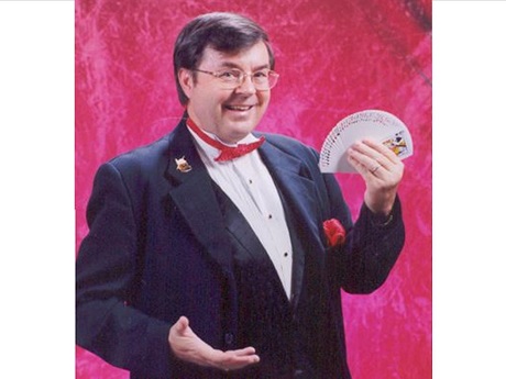 Glen Bailey in a tuxedo and red bow time fanning a deck of cards