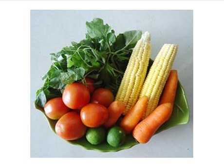 Photo of bowl containing 2 ears of corn, 4 carrots, 6 tomatoes, 2 avocados, and leafy vegetables.