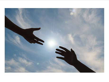 Photo of 2 hands reaching toward each other against a background of blue sky and white clouds.