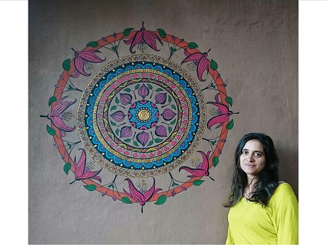 Artist Ayala Wise standing in front of a red, aqua and purple mandala painted on a wall