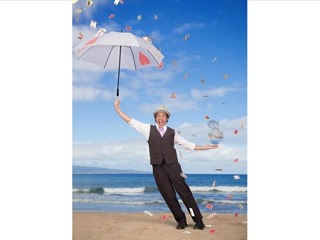 man with umbrella standing on beach with cards flying all around