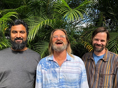 Three bearded men laughing with a background of areca palms