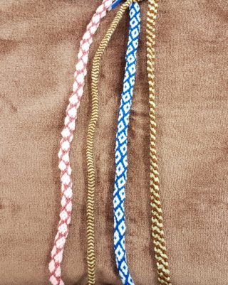 four kumihimo cords in pink, red, brown, cream, blue and white. Set against a brown background