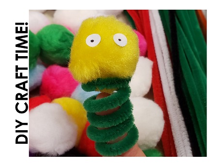 Example of pipe cleaner finger puppet made of yellow poof ball and green pipe cleaner against a backdrop of craft supplies