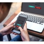 Man holding smartphone with laptop on table