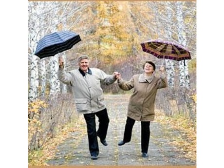 two older adults holding umbrellas dance on a path outside
