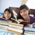 Two girls reading books on a bed
