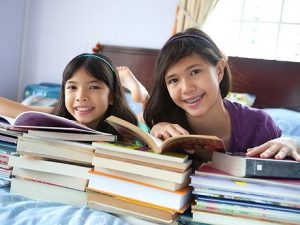 Two girls reading books on a bed