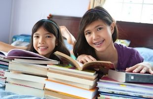 Two girls reading books on a bed