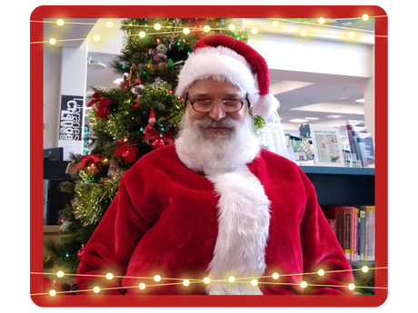 Santa sitting in front of a Christmas tree in the library