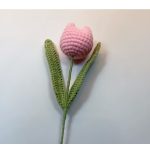 A crocheted pink tulip with green leaves and stem