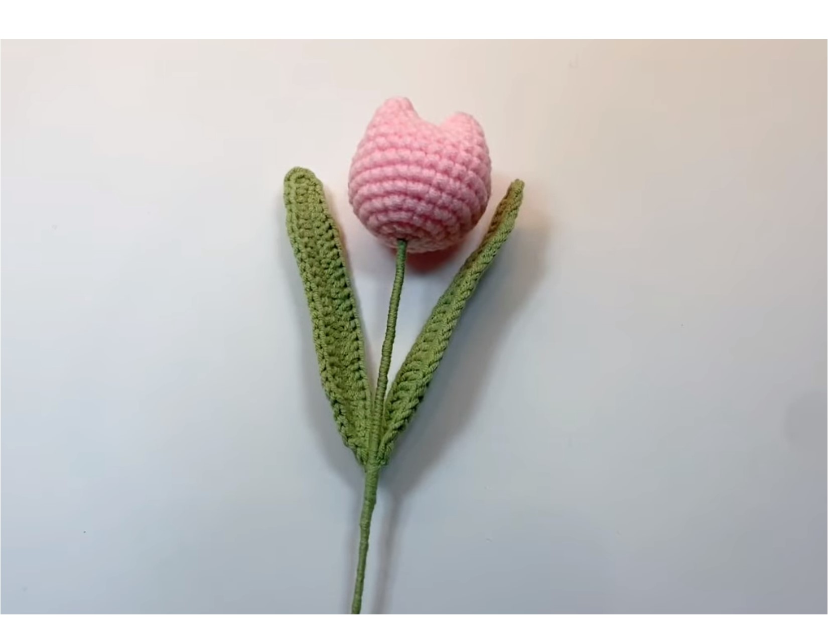 A crocheted pink tulip with green leaves and stem