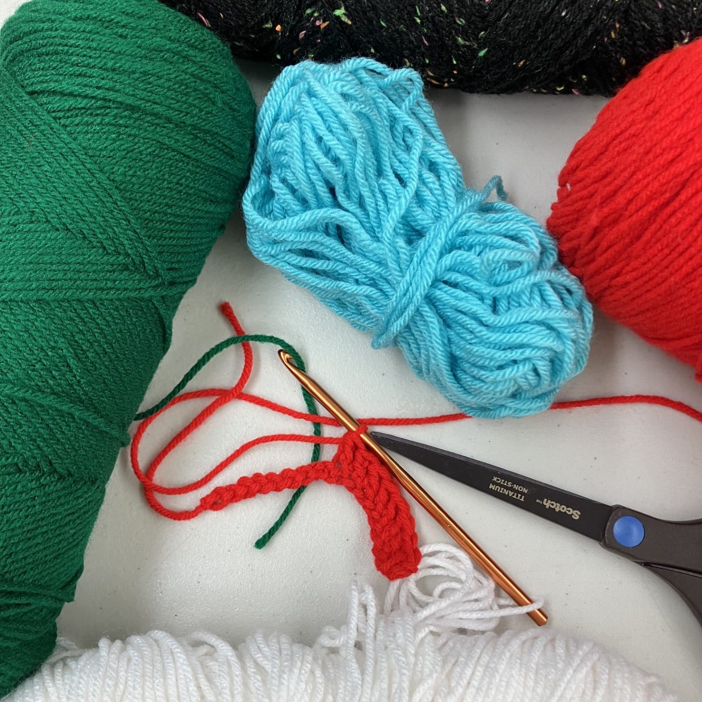 assortment of yarns in different colors with a pair of scissor and crochet needle starting a project