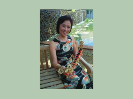 An Asian woman sitting on a bench and holding Chinese knotwork.