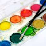 tray of watercolors with two brushes. Colors yellow, orange, red, blue, green, mustard, brown. etc