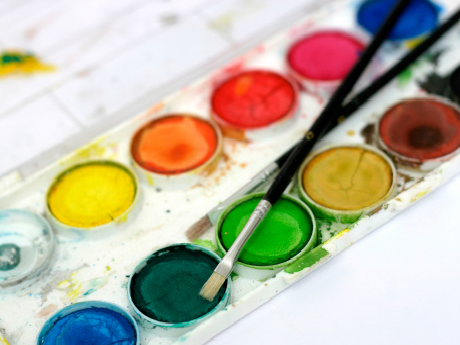 tray of watercolors with two brushes. Colors yellow, orange, red, blue, green, mustard, brown. etc