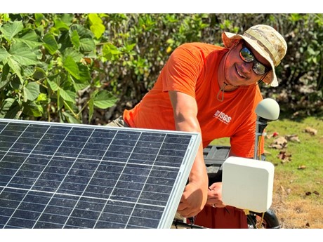 Scientist conducting maintenance on solar panel and seismic instrument among green foliage