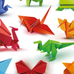 A red dragon, an orange and a yellow crane, and a green dinosaur, all made out of origami paper, surrounded by other creations, on a white background.