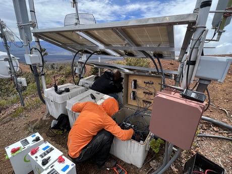 A Hawaiian Volcano Observatory technician replaces batteries at a monitoring station located on Hualālai. The station is powered by batteries that store energy generated by solar panels.