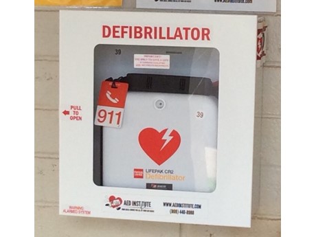 A white and red Automated External Defibrillator (AED) machine in a box mounted on a wall.