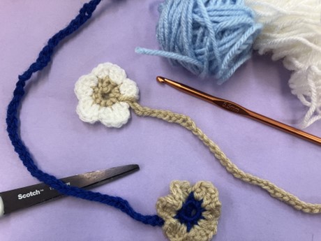 two crocheted flower bookmarks with a scissor, yarn balls, and crochet hook