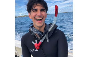 Man wearing a wetsuit and snorkel, smiling broadly at the camera