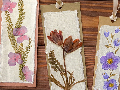 Three pressed flower bookmarks. Purple flowers are on the right, the middle has red flowers, and the left has pink.