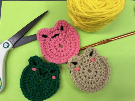 3 crocheted frog coasters with crochet hook, scissors and yarn