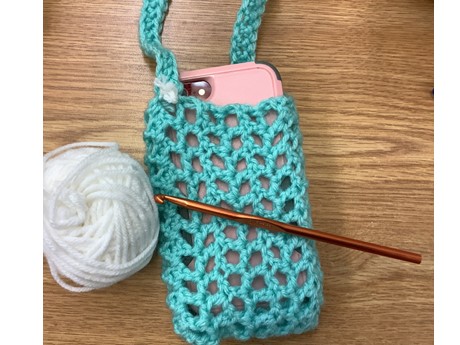 mesh crocheted bag carrying a phone with yarn and crochet hook
