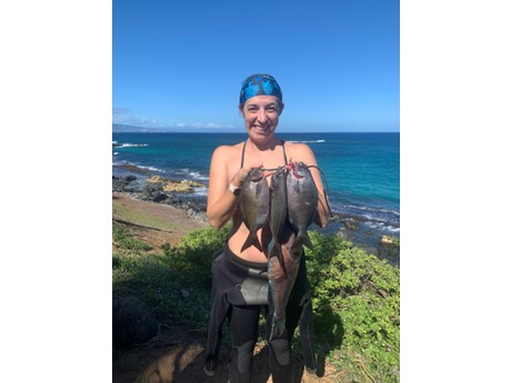 A woman carrying a string of fish at a beach.