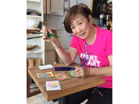 An Asian woman in a pink shirt holding a paintbrush