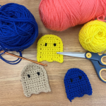 various colors of crocheted ghosts with yarn and scissor