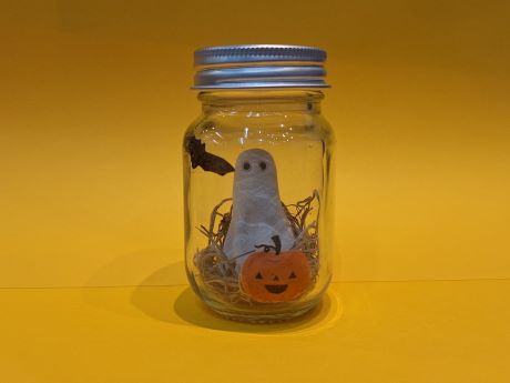A small clay ghost with moss in a jar. The jar is decorated with a bat and pumpkin