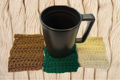 a black mug on a green crochet coaster with a brown coaster on the left and a white coaster on the right. Background is hanks of white yarn.