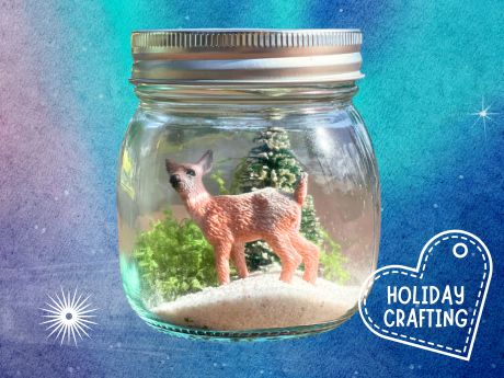 Mason jar filled with deer figurine standing on artificial snow. Pine tree and moss in the background.