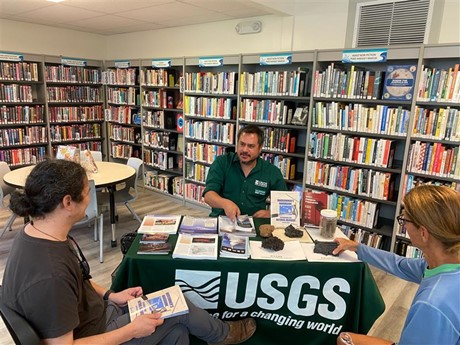 USGS photo: Kevan Kamibayashi talks story in library with two patrons at table during Volcano Awareness Month last year, 2024