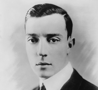 Photo of actor Buster Keaton as a young man. He has large dark eyes, slicked back hair, and is wearing a dark suit and tie.