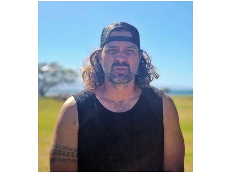 Headshot of Kalaniua Ritte, a Hawaiian man, dressed in a black tank top and wearing a backwards black hat.