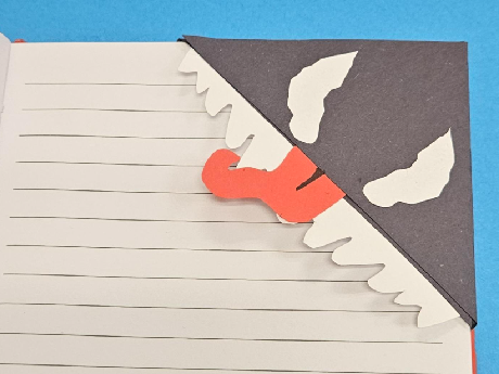 blue background, lined paper with a black corner on the top right corner and white eyes and teeth, and a red tongue