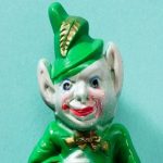 A creepy ceramic leprechaun with grey skin and bat ears, dressed in a green suit.