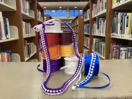 Spools of ribbon stacked up with woven ribbon lei draped over the spools