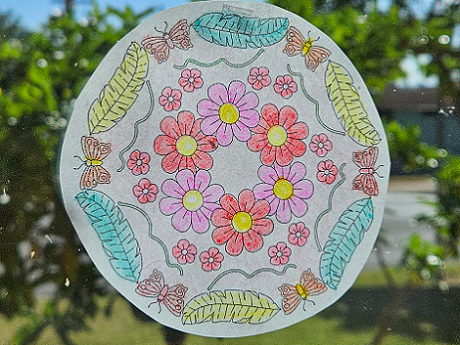 a circle of paper colored in and hanging on a window with gardenia leaves in the background