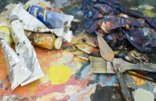 Paints, brushes, and painting knives are strewn across a dirty pallet.