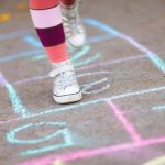 Legs of a person in white sneakers playing hopscotch on sidewalk.