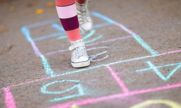 Legs of a person in white sneakers playing hopscotch on sidewalk.